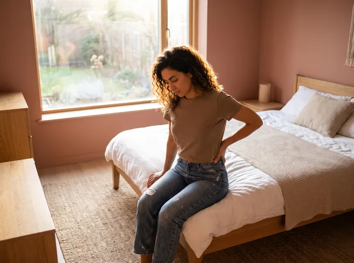 Patient sitting on the edge of the bed holding their low back in the morning