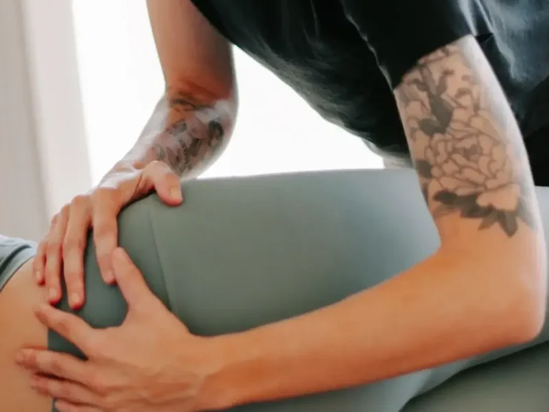 Tattooed forearms and hands pressing gently into a patient's hip