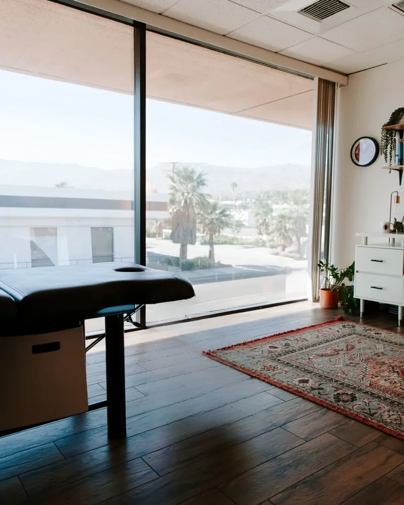 Treatment table, Persian rug and floor to ceiling window onto desert palms